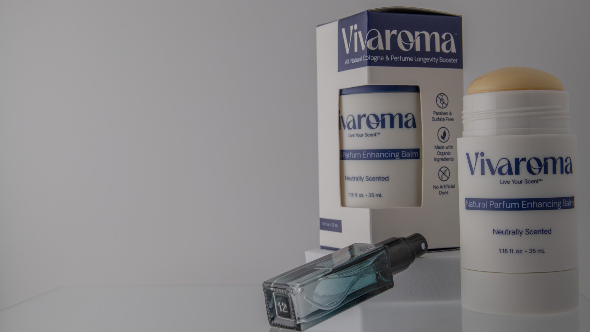 Vivaroma perfume enhancing balm product display featuring a white and blue cardboard box, a white cylindrical balm container with a beige stick top, and a small clear glass spray bottle on a light gray background.